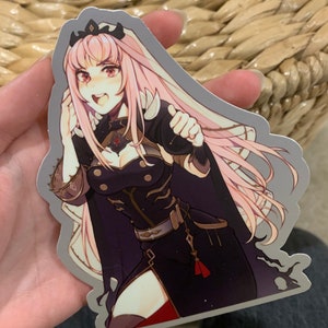 May include: A sticker featuring a pink-haired anime character with red eyes, wearing a black and gold outfit. The character is holding a sword and has a determined expression.
