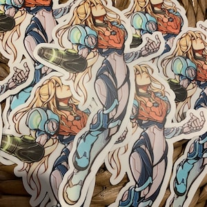 May include: A set of five stickers featuring a female character in a blue and white suit with long blonde hair. The character is holding a weapon in her right hand and has a determined expression on her face.