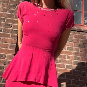 May include: A bright pink dress with a fitted bodice and a flowing skirt. The dress has a beaded neckline and short sleeves.