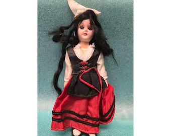 Mini muñeca de porcelana vintage con traje folclórico tradicional rojo y negro con detalles de encaje y sombrero blanco.