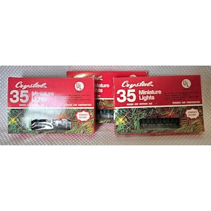 Könnte beinhalten: Drei rechteckige Schachteln mit 35 Miniatur-Lichtern der Marke Crystal. Die rote Verpackung zeigt weißen Text, ein UL-Logo und ein Bild von Tannenzweigen. Jede Schachtel weist auf den Innen- und Außenbereich sowie Energieeinsparung hin.