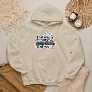 May include: A beige hooded sweatshirt featuring a graphic print with the text That wasn't very data-driven of you. The design includes colorful icons of a spreadsheet, bar charts, and a pie chart, all centered on the front of the garment.
