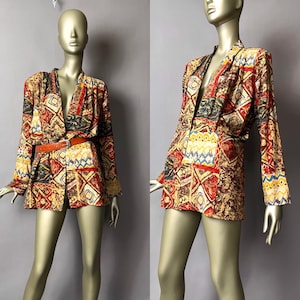 May include: A patterned blazer with a brown belt. The blazer features a mix of geometric shapes in red, yellow, blue, and black. The long-sleeved jacket is displayed on a mannequin.