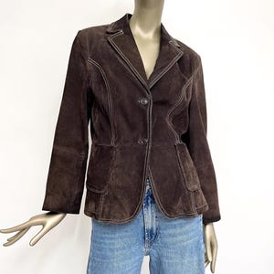 Puede incluir: Una chaqueta de ante marr&oacute;n con costuras blancas. La chaqueta tiene un cuello de muesca, cierre de bot&oacute;n y dos bolsillos de solapa.