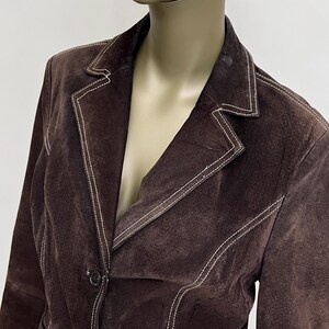 Puede incluir: Una chaqueta de ante marr&oacute;n con costuras blancas. La chaqueta tiene un cierre de bot&oacute;n &uacute;nico y un cuello.