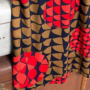 May include: A fabric garment featuring a dark navy blue background with a repeating pattern of brown semi-circular shapes and large, vibrant red circular motifs composed of smaller geometric segments arranged in a dense, abstract graphic design.