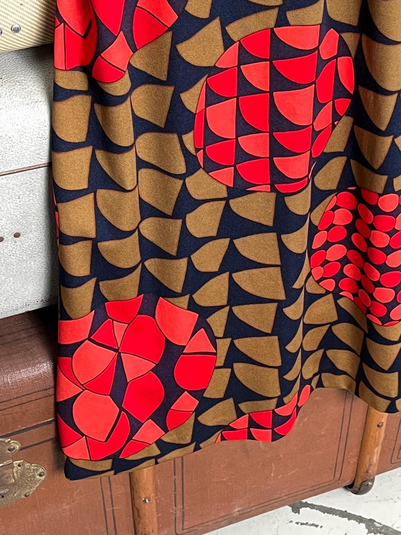 May include: A fabric garment featuring a dark navy blue background with a repeating pattern of brown semi-circular shapes and large, vibrant red circular motifs composed of smaller geometric segments arranged in a dense, abstract graphic design.