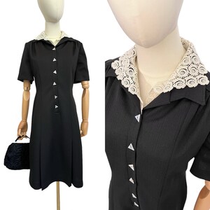 May include: A black dress with a white lace collar and button closure. The dress has short sleeves and a slightly flared skirt.