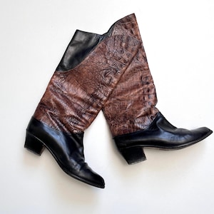 以下が含まれることがあります： ヴィンテージのニーハイブーツのペア。ブーツは、黒革と茶色のテクスチャード加工された素材を組み合わせており、爬虫類の皮膚に似せるためにエンボス加工されている可能性があります。ブーツはローヒールで、つま先が尖っています。