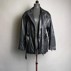 May include: A black leather jacket with a notched collar, zipper closure, and belt detail. The jacket is displayed on a mannequin and has a classic, vintage style. The jacket has a shiny finish and appears to be in good condition.