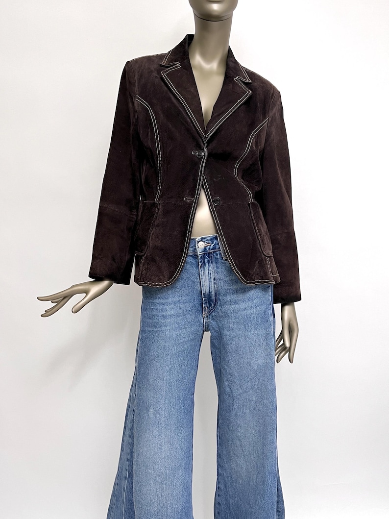 Puede incluir: Una chaqueta de ante marr&oacute;n con costuras blancas. La chaqueta tiene un cuello de muesca, cierre de dos botones y dos bolsillos delanteros.