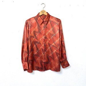 Könnte beinhalten: Ein langärmliges Hemd mit Knöpfen und einem geometrischen Muster in Orange- und Schwarztönen.