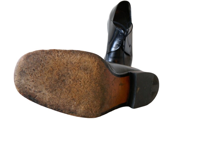 May include: Black leather dress shoe with a lace-up closure. The shoe has a brown leather sole and a rubber heel.