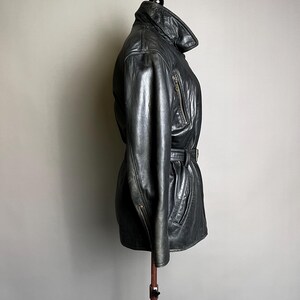 May include: Black leather jacket with a belted waist and a high collar. The jacket has a zipper closure and two front pockets. The jacket is displayed on a mannequin.