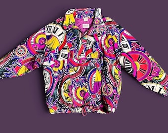 May include: A long-sleeve pullover jacket featuring a vibrant, multi-colored pattern of clock faces, Roman numerals, and floral motifs in shades of pink, yellow, blue, and black. The jacket has a high collar, a front zipper, and a drawstring hem.