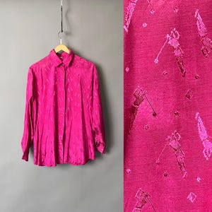Könnte beinhalten: Ein leuchtend pinkfarbenes Langarmhemd hängt an einem Holzbügel. Das Hemd hat ein strukturiertes Muster. Eine Nahaufnahme zeigt ein Golf-Motiv auf dem Stoff mit Golfspielern in Aktion.
