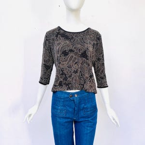 Könnte beinhalten: Ein schwarzes Oberteil mit goldfarbenem Paisley-Muster und 3/4-Ärmeln. Das Oberteil ist aus dehnbarem Stoff und hat einen runden Ausschnitt.