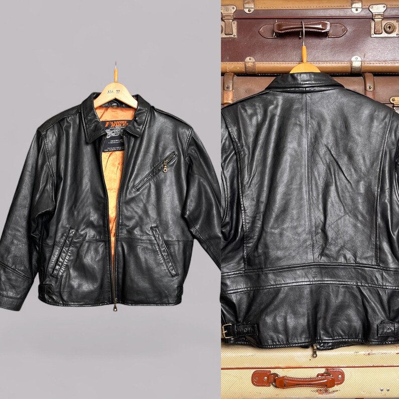 May include: A black leather jacket with a collared neckline, front zipper, and multiple pockets. The jacket has a gold-colored interior lining and is displayed on a wooden hanger. The back of the jacket is also shown, with a belt detail at the waist.