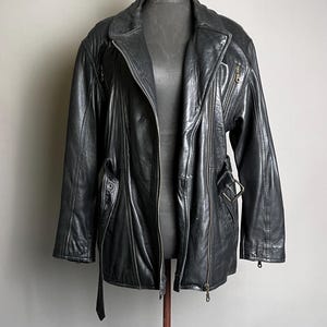 May include: A black leather jacket with a zipper closure, side pockets, and a belt detail. The jacket is displayed on a mannequin against a neutral background. The jacket has a classic biker style.