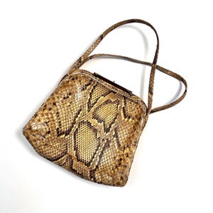 Könnte beinhalten: Eine kleine, braune und beigefarbene Schlangenledertasche mit einem Verschluss und einem einzigen Trageriemen.
