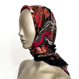 Può includere: Una sciarpa quadrata con un motivo floreale e paisley. La sciarpa presenta uno sfondo nero con disegni floreali rossi, arancioni e marroni e un bordo paisley. La sciarpa è drappeggiata su una testa di manichino.