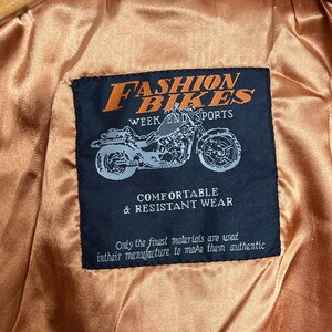 May include: Black leather jacket interior with a label that reads "FASHION BIKES WEEK END SPORTS". The label also features a motorcycle graphic and the text "COMFORTABLE & RESISTANT WEAR". The jacket size is 36.