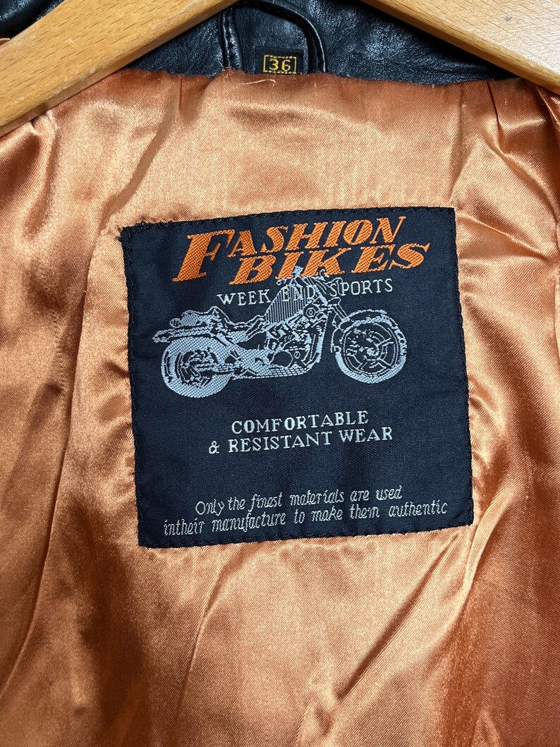 May include: Black leather jacket interior with a label that reads "FASHION BIKES WEEK END SPORTS". The label also features a motorcycle graphic and the text "COMFORTABLE & RESISTANT WEAR". The jacket size is 36.