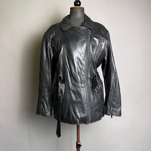 May include: A dark gray leather jacket with an asymmetrical zipper closure, multiple zippered pockets, and a belted waist. The jacket is displayed on a mannequin and has a classic biker style.