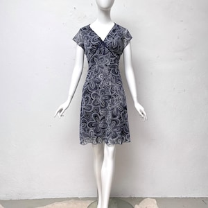 May include: A short, navy blue dress with a white floral pattern. The dress has a v-neckline and short sleeves.