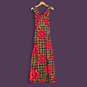 May include: A sleeveless maxi dress featuring a V-neckline and a repeating geometric pattern of tan semicircles on a dark navy background, accented with large, circular motifs filled with red and pink segmented shapes throughout the garment.