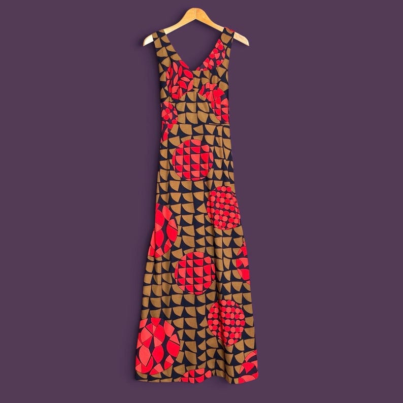 May include: A sleeveless maxi dress featuring a V-neckline and a repeating geometric pattern of tan semicircles on a dark navy background, accented with large, circular motifs filled with red and pink segmented shapes throughout the garment.
