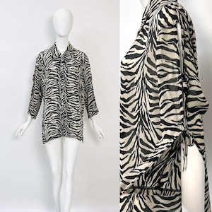 Pode incluir: Uma camisa transparente de manga comprida com botões e estampa de zebra. A camisa tem um laço no pescoço e fendas nas laterais.