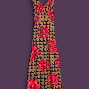 May include: A sleeveless floor-length dress featuring a V-neckline and a repeating geometric pattern. The design consists of dark navy blue semicircles on a tan background, accented by large circular motifs filled with bright red and pink segments.