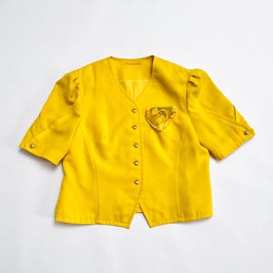 May include: A yellow short-sleeved blazer with a button-up front and a small floral design on the left side.