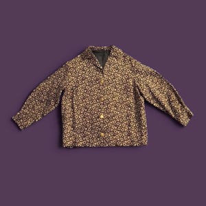 May include: A long-sleeved button-down jacket featuring a dark brown and cream-colored circular floral pattern. The garment has a pointed collar, a straight hemline, and four gold-toned circular buttons running down the center front placket.