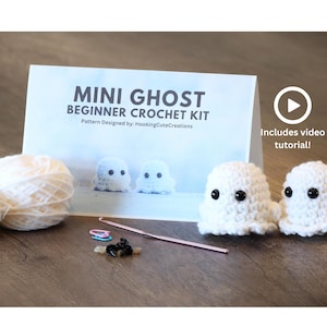 May include: A crochet kit for making mini ghost figures. The kit includes white yarn, stuffing, a crochet hook, stitch markers, and black safety eyes. The kit also includes a printed guide and a video tutorial. The text on the guide reads "MINI GHOST BEGINNER CROCHET KIT".