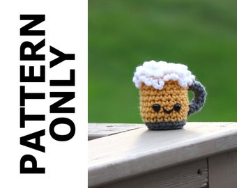 May include: A crocheted beer mug with a white foam top and a smiling face. The mug is sitting on a wooden surface.