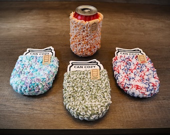 May include: Four crocheted can cozies in different colors: blue and white, green and white, red and white, and orange and white. Each cozy has a tag that says "CAN COZY".
