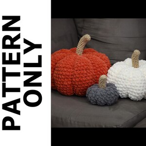 May include: Three crocheted pumpkins in different sizes and colors: orange, white, and gray. The pumpkins are sitting on a gray couch.