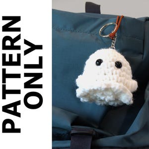 May include: A white crocheted ghost keychain with black button eyes hangs from a silver keyring. The keychain is attached to a teal backpack. The text "PATTERN ONLY" is printed vertically on the left side of the image.