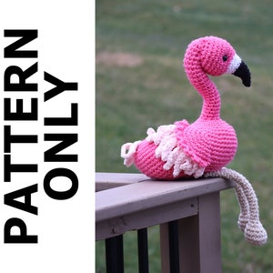 May include: A pink crocheted flamingo with a black beak and white eyes. The flamingo is sitting on a wooden railing with its legs hanging down.