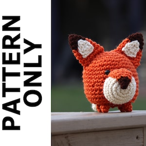 Puede incluir: Un juguete de amigurumi de zorro tejido a crochet con pelaje naranja, blanco y marrón. El juguete tiene un cuerpo redondo y pequeñas patas.