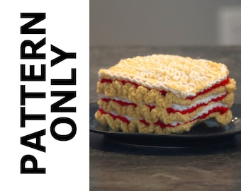 May include: A crocheted layered cake with yellow, white, and red frosting. The cake is on a blue plate.