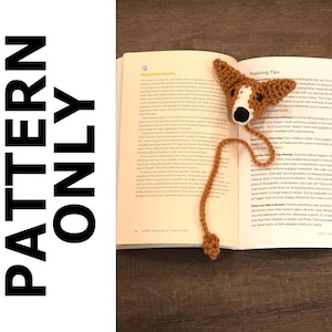 Puede incluir: Un marcapáginas de perro de ganchillo en marrón y blanco con una cola larga. El marcapáginas está colocado en un libro abierto con el texto "Training Tips" visible.