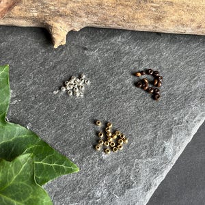 Mach dein Armband persönlich: wähle zwischen Holz-Messing- oder Metallperlen aus. Wenn du es ganz schlicht magst, kannst du auch statt den Perlen ein Knoten auswählen.