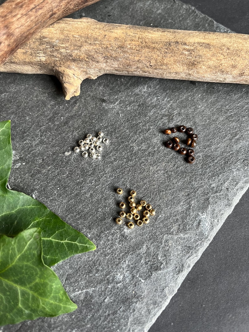 Mach dein Armband persönlich: wähle zwischen Holz-Messing- oder Metallperlen aus. Wenn du es ganz schlicht magst, kannst du auch statt den Perlen ein Knoten auswählen.