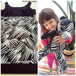 May include: A black and white zebra print dress with a black bodice and a zebra print skirt. The dress is sleeveless and has a scoop neck. A young girl is holding a zebra print stuffed animal.