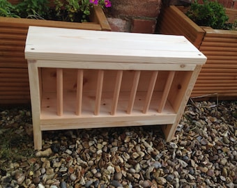 May include: A wooden dish rack with a slatted front and a solid top. The rack is made of natural wood and is sitting on a bed of gravel.