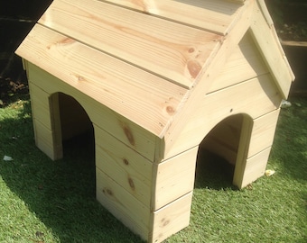 May include: A light-colored wooden pet house featuring a gabled roof and two arched openings on the front and side. The structure is constructed from horizontal planks with visible wood grain and knots, showcasing a natural, unfinished light wood finish.