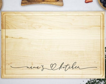 May include: A large wooden cutting board with the text "nana's kitchen" engraved on it. The board is surrounded by various kitchen items, including a bowl of sugar, a butter dish, a bowl of blueberries, and strawberries.